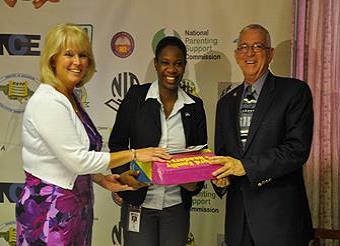 Hon. Ronald Thwaites, Minister of Education, and Denise Herbol, USAID Mission Director in Jamaica, accept books for the Camp from Alicia Young of JNBS